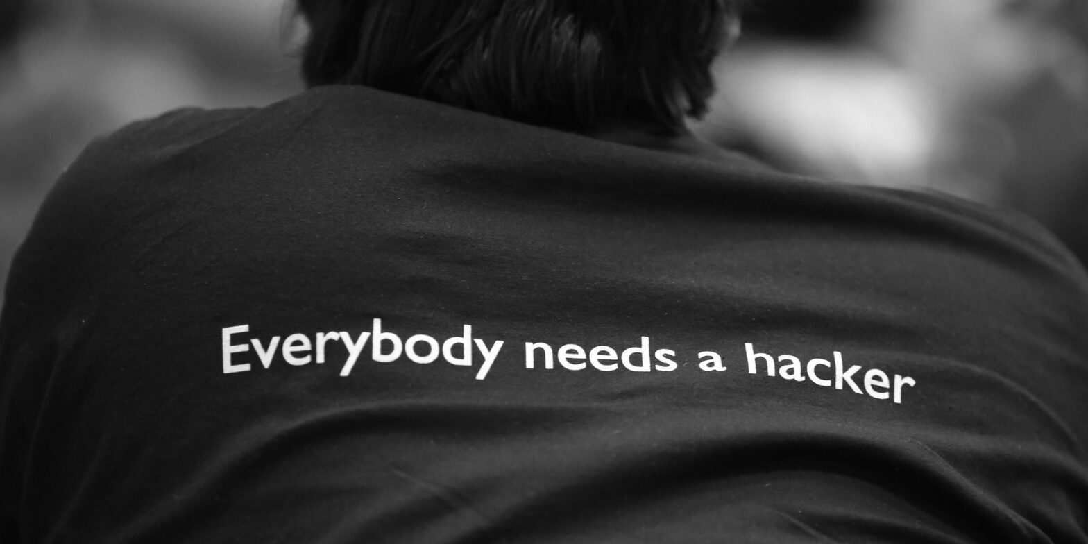 Un tipo di spalle con una maglia nera sulla quale è scritto Everybody needs a hacker