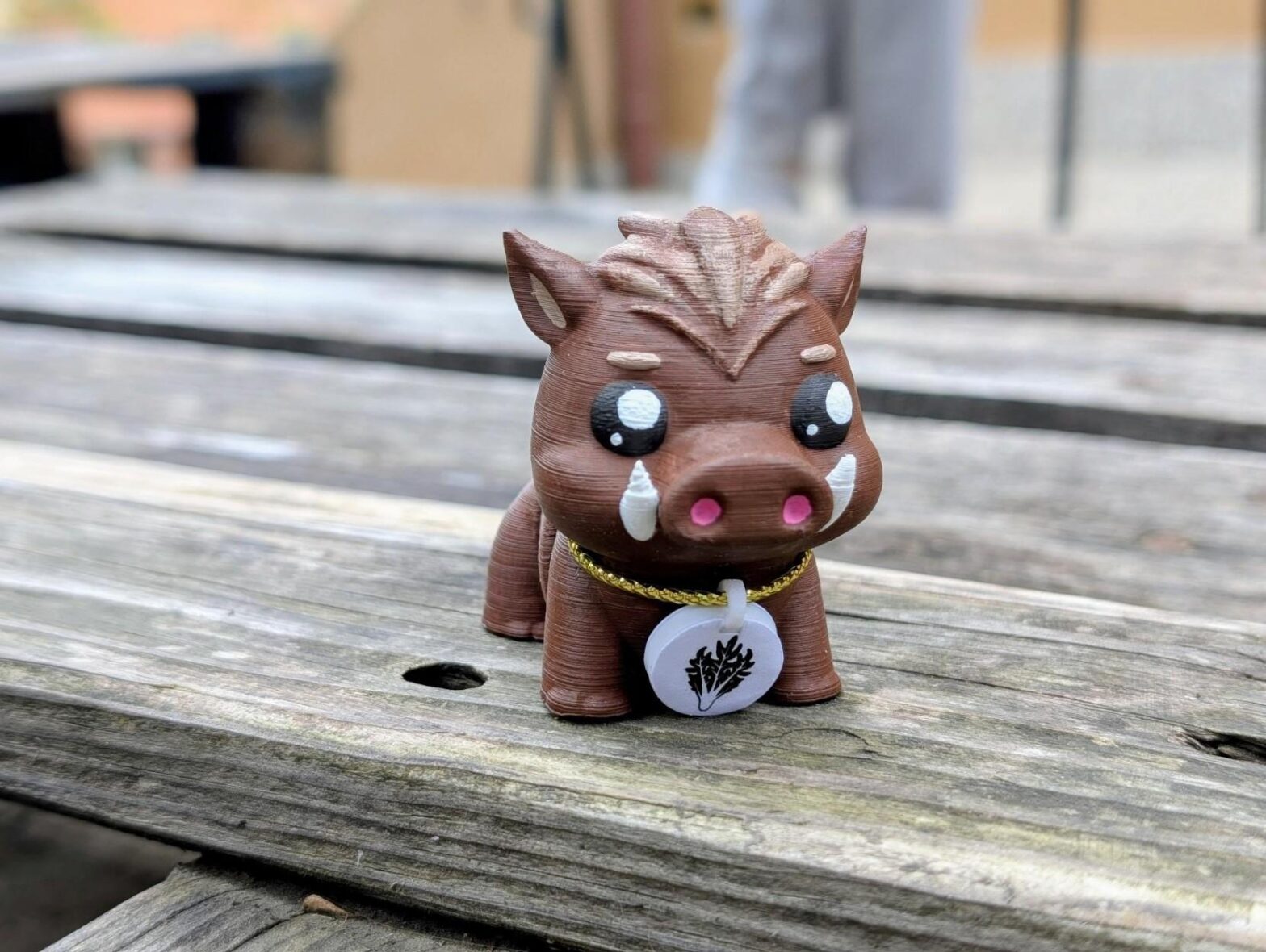 Un piccolo cinghiale stampato in 3d con il medaglione di puntarella poggiato su un tavolo di legno
